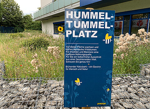 Ein Schild mit der Erklärung zum Hummel-Tummel-Platz vor dem Kundenzentrum von Streck Transport in Freiburg